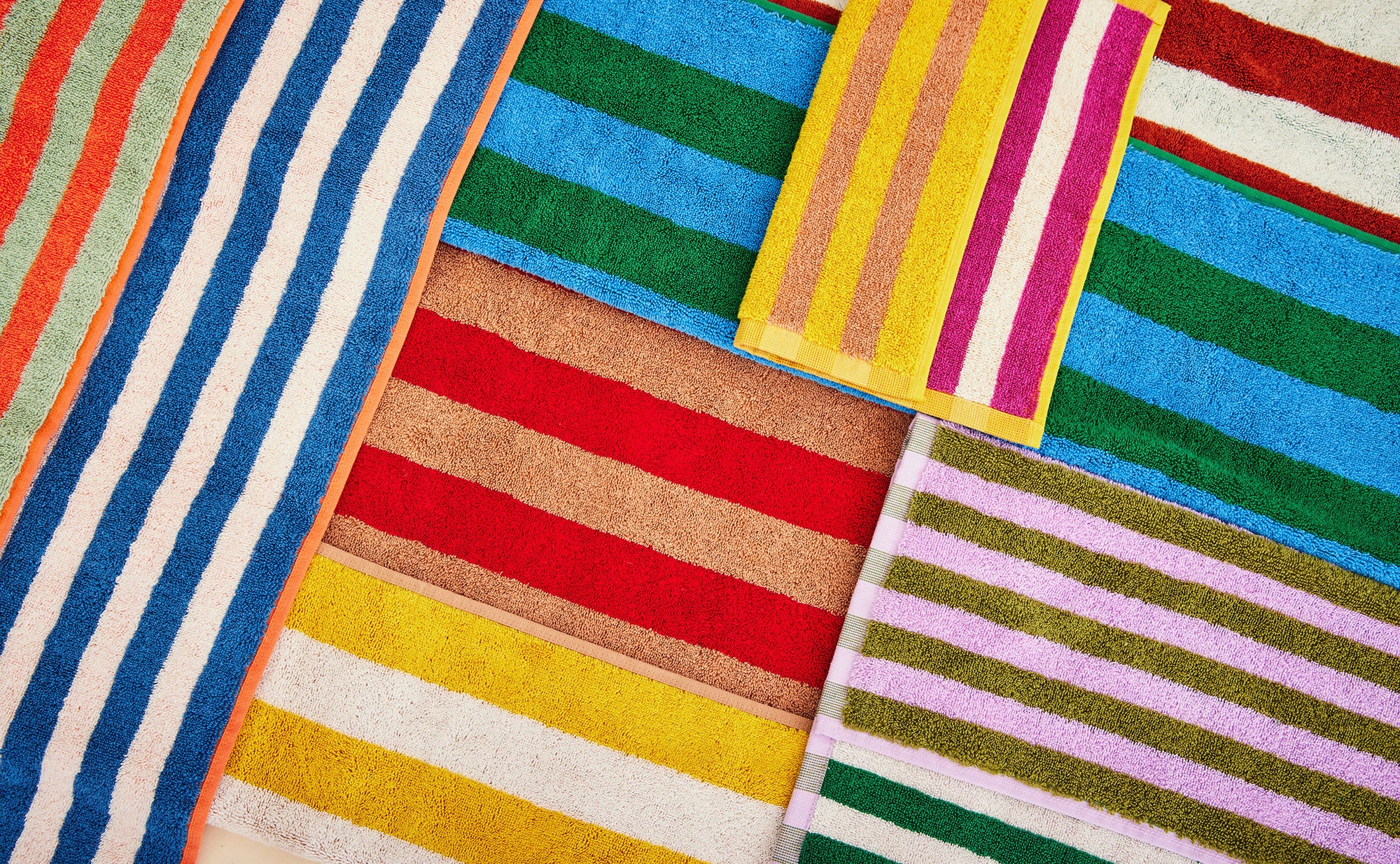 Dusen Dusen orange, green, red, brown purple, yellow stripe bath and hand towels laid down together in an abstract composition.