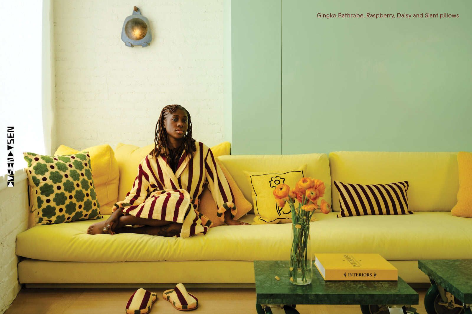 Kara Jackson sitting on yellow couch in Ginkgo Robes with Raspberry Daisy and Slant pillows
