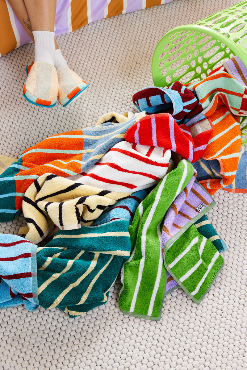 Striped towels of all colors coming out a hamper. Feet wearing slippers behind them.
