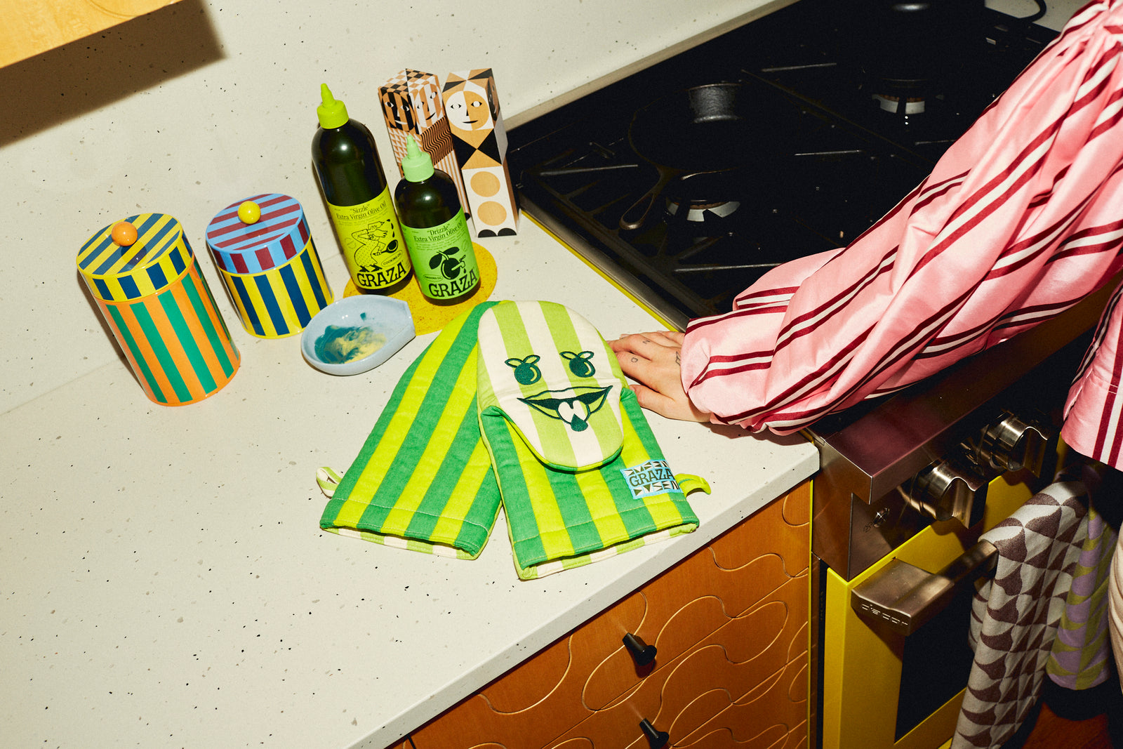 green oven mitt on counter with graza olive oil