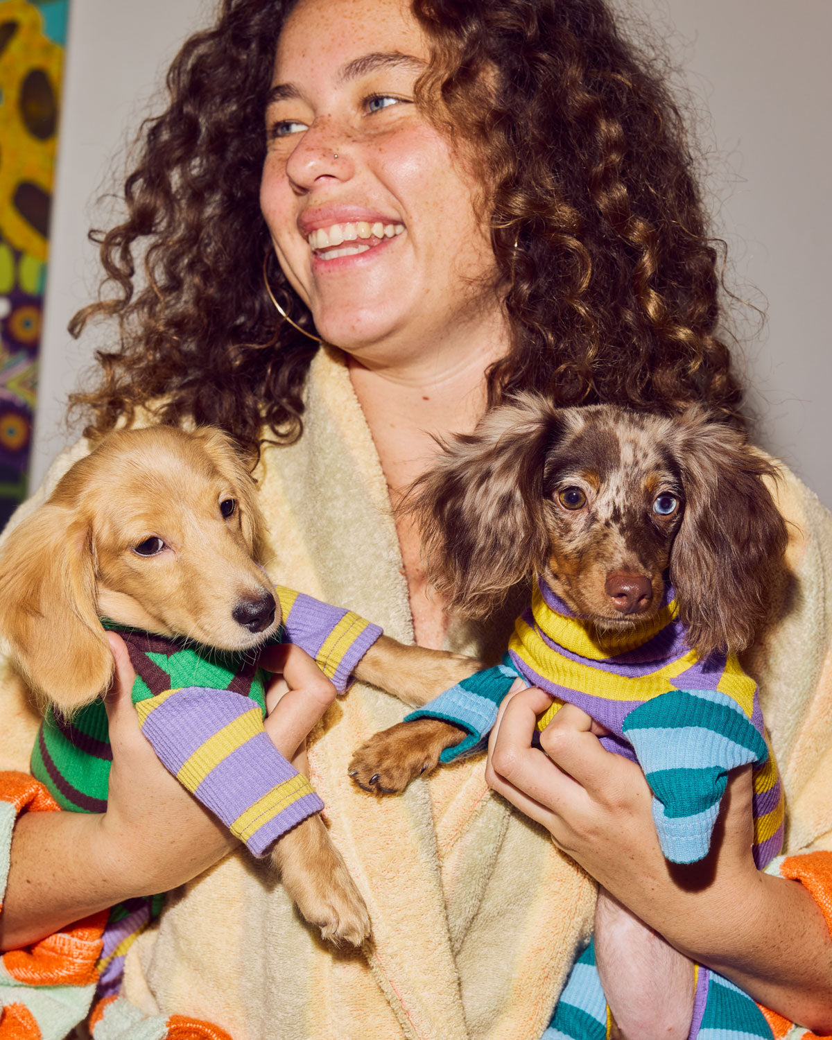 Two dachshunds are held by a smiling woman wearing a white and green onesie