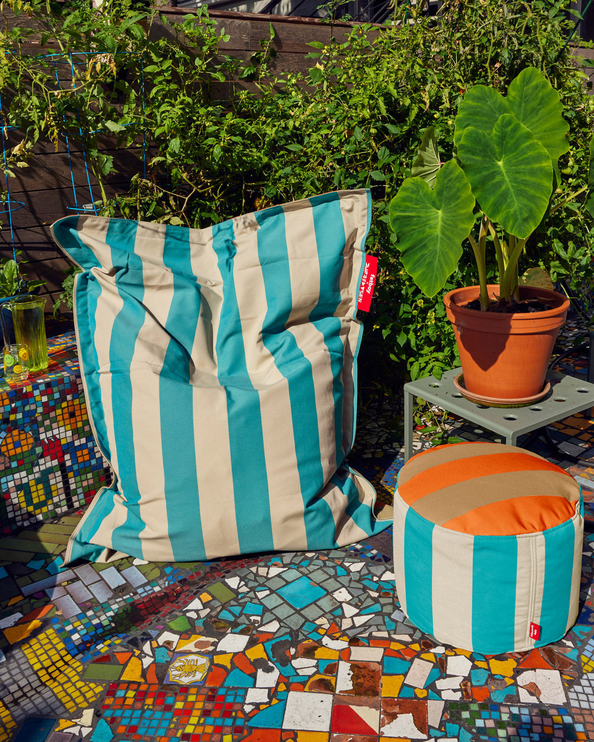 Fatboy x Dusen Dusen Outdoor Outdoor Slim Classic Bean Bag Chair in Stripe and Oak. One in Dark Brown and Orange, the other in white and blue based on the ground and sky. The other pattern in a rust and beige oak pattern. Stripe bean bag with pouf and plant