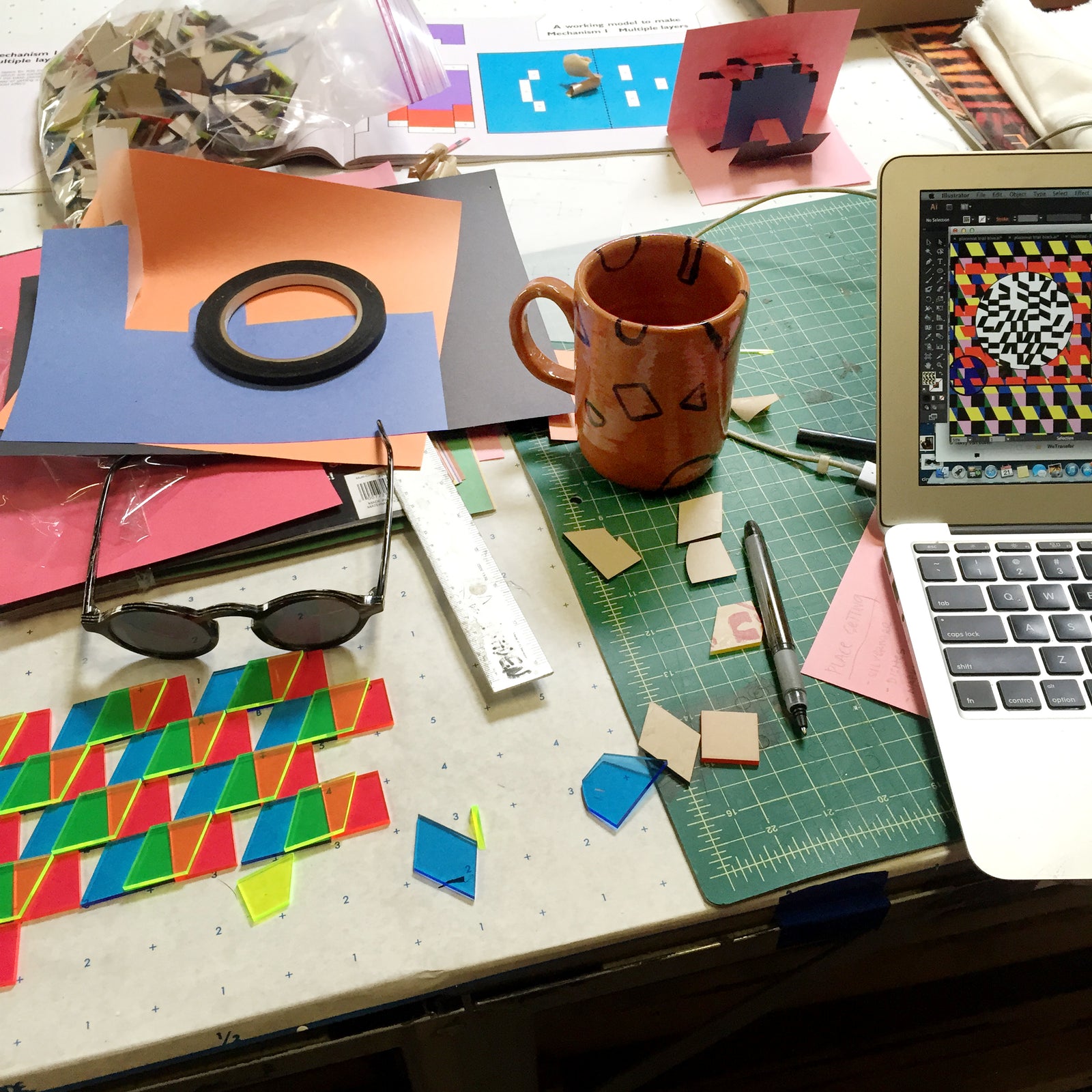 resin shapes on desk with computer rendering mug and other work materials