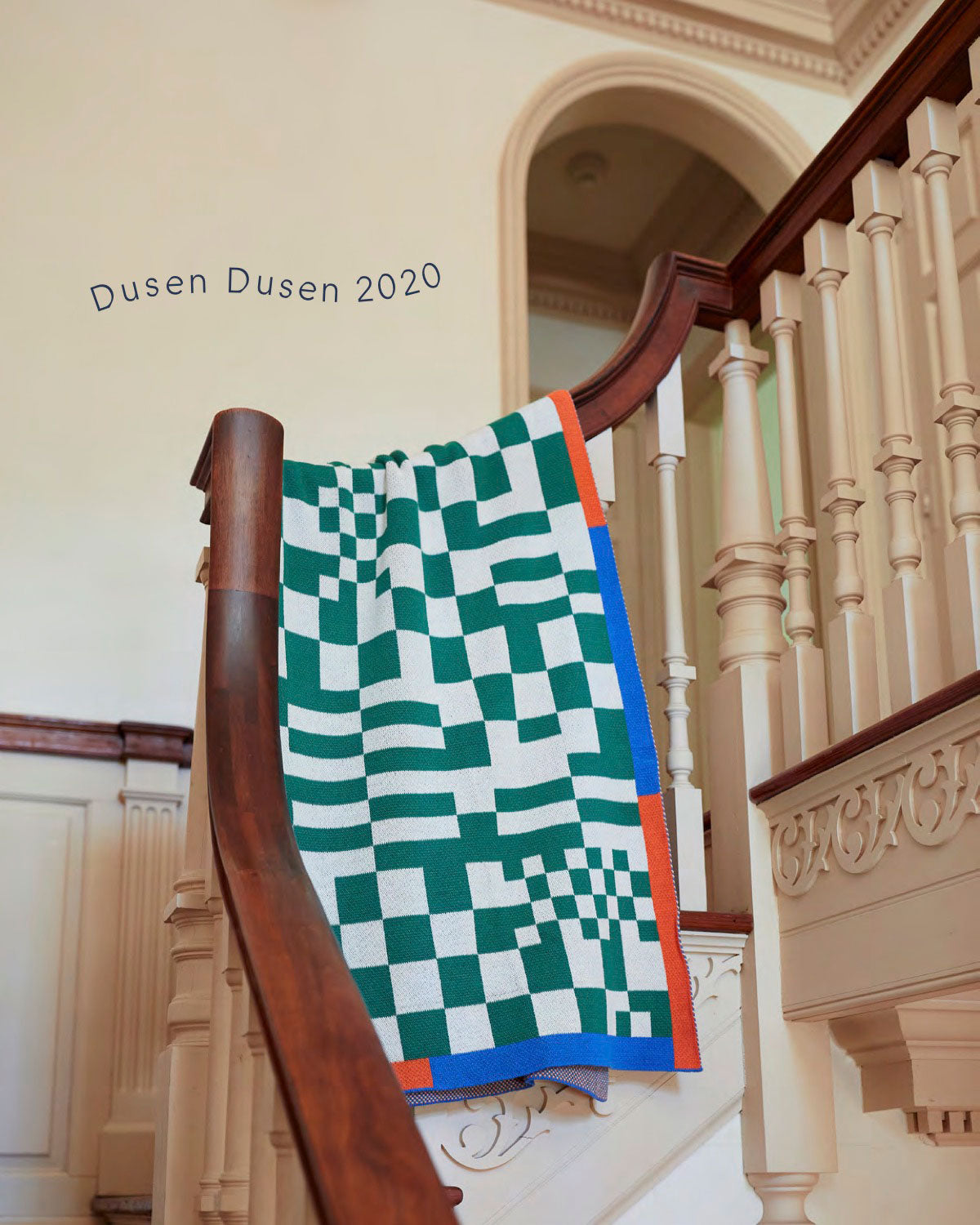 Green checked blanket over railing over Dusen Dusen 2020 text