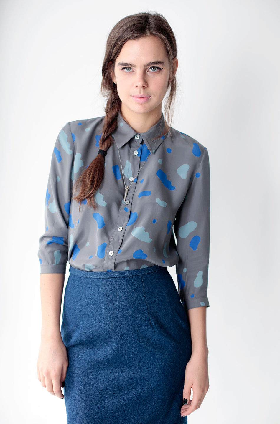 woman in grey button up shirt with blue splotch pattern and blue denim penicl skirt
