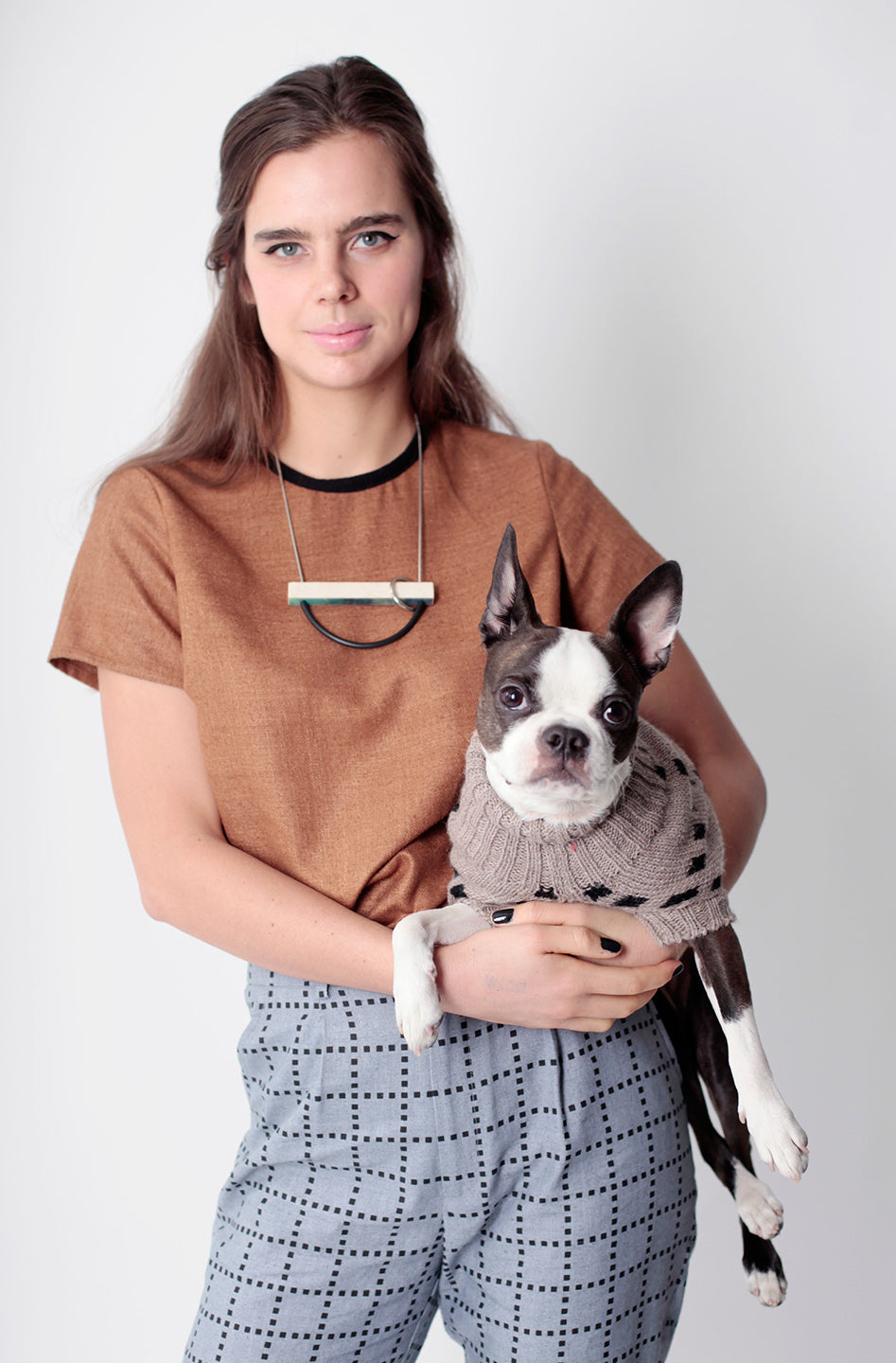 snips in brown sweater being held by woman in brown top with grey grid pants