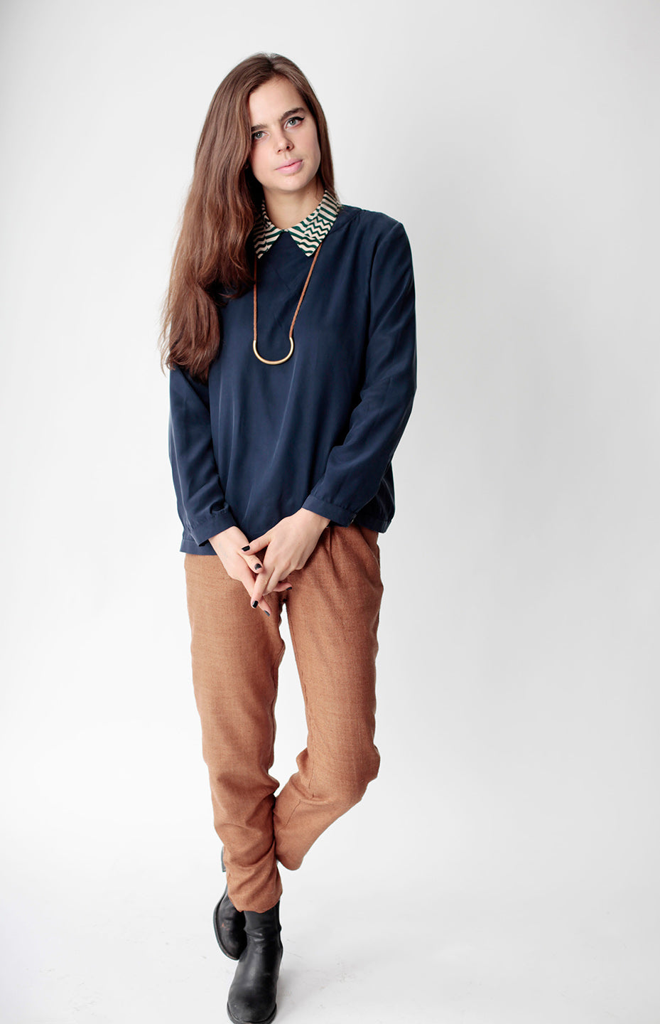 model in blue shirt with squiggle collar long arc necklace and tan pants