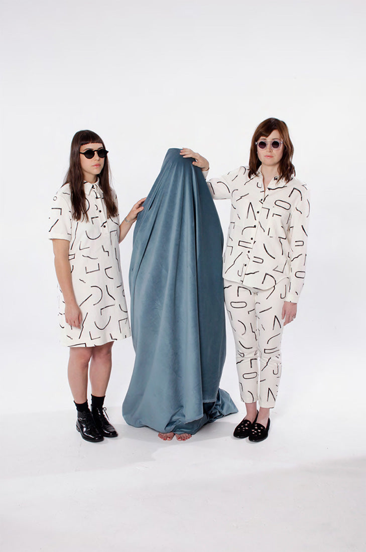 two models in white with black line pattern clothing, one in dress and other in top and pants
