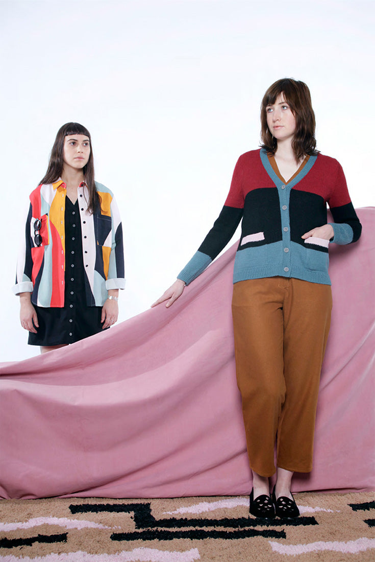 model in stripe cardigan, tan pants and another behind her in colorful button up with black button up dress