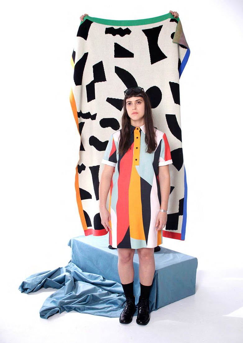 model in button up collared dress with strong colorblock pattern in front of block pattern throw