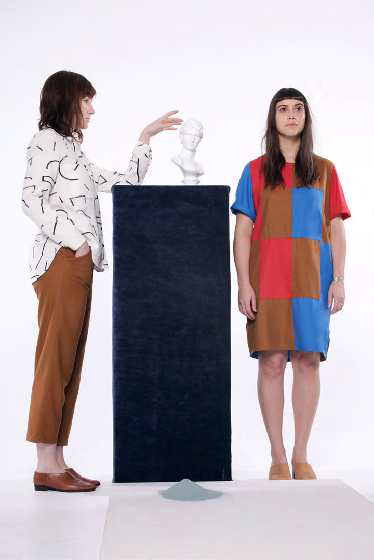model in white shirt with black ine pattern , tan pants and model in tan red blue checked dress