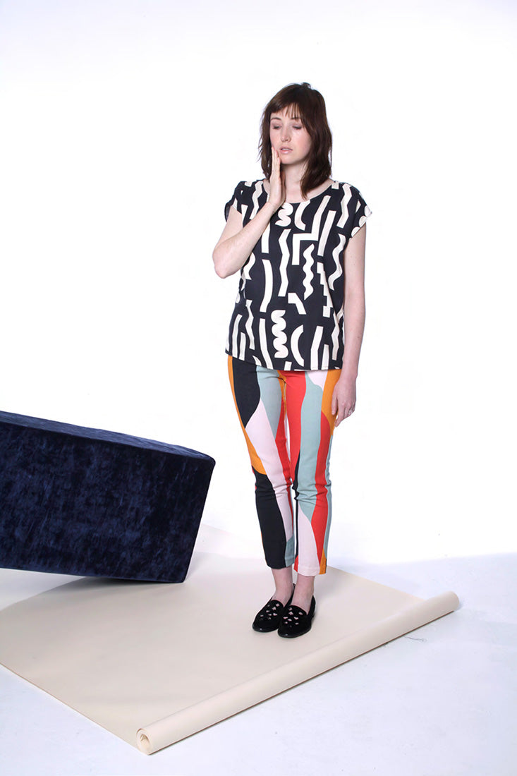 model in black top with white squiggle and colorful print pants hand on cheek