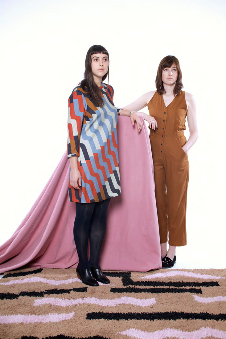 model in pattern dress with black tights and another model in tan fitted romper
