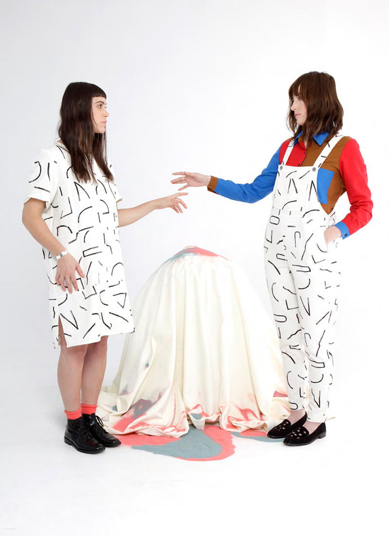 model in white dress with black line pattern and model in same pattern overalls gesturing towards one another