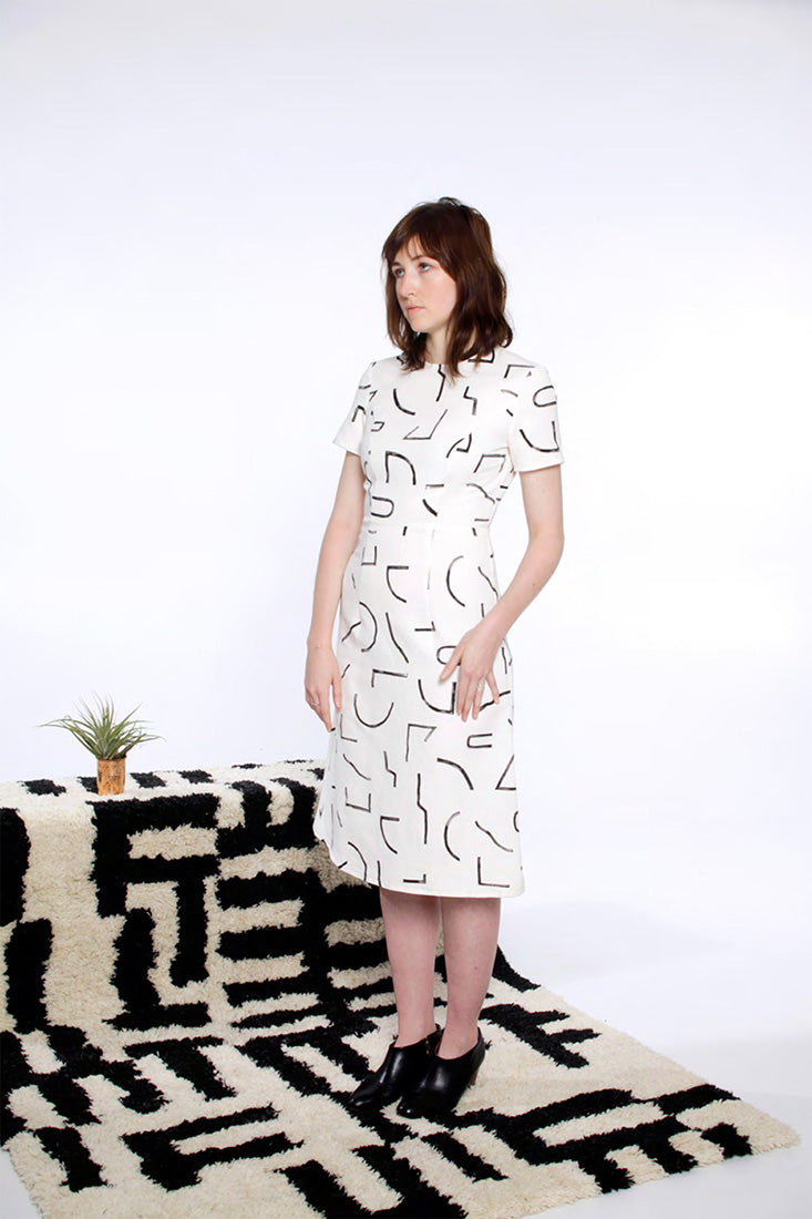 model in white dress on rug with black line pattern