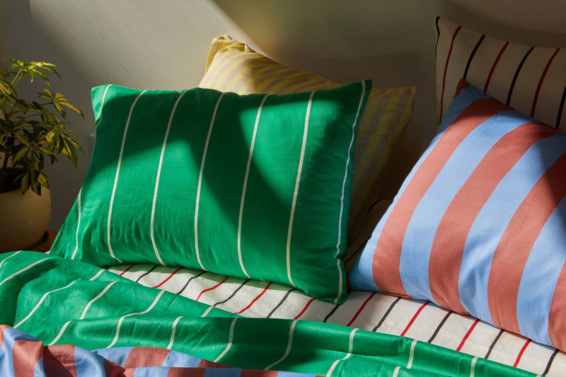 Dusen Dusen Lawn Stripe Sheets. Sheeting in green and white stripes. 100% cotton sateen, 300 thread count. Machine wash cold and tumble dry. with many other stripes on a bed in natural light