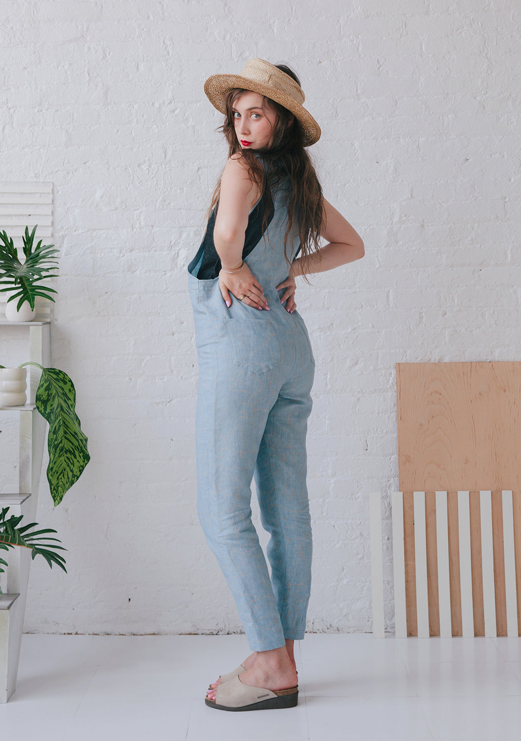 woman in denim overalls from behind with straw visor