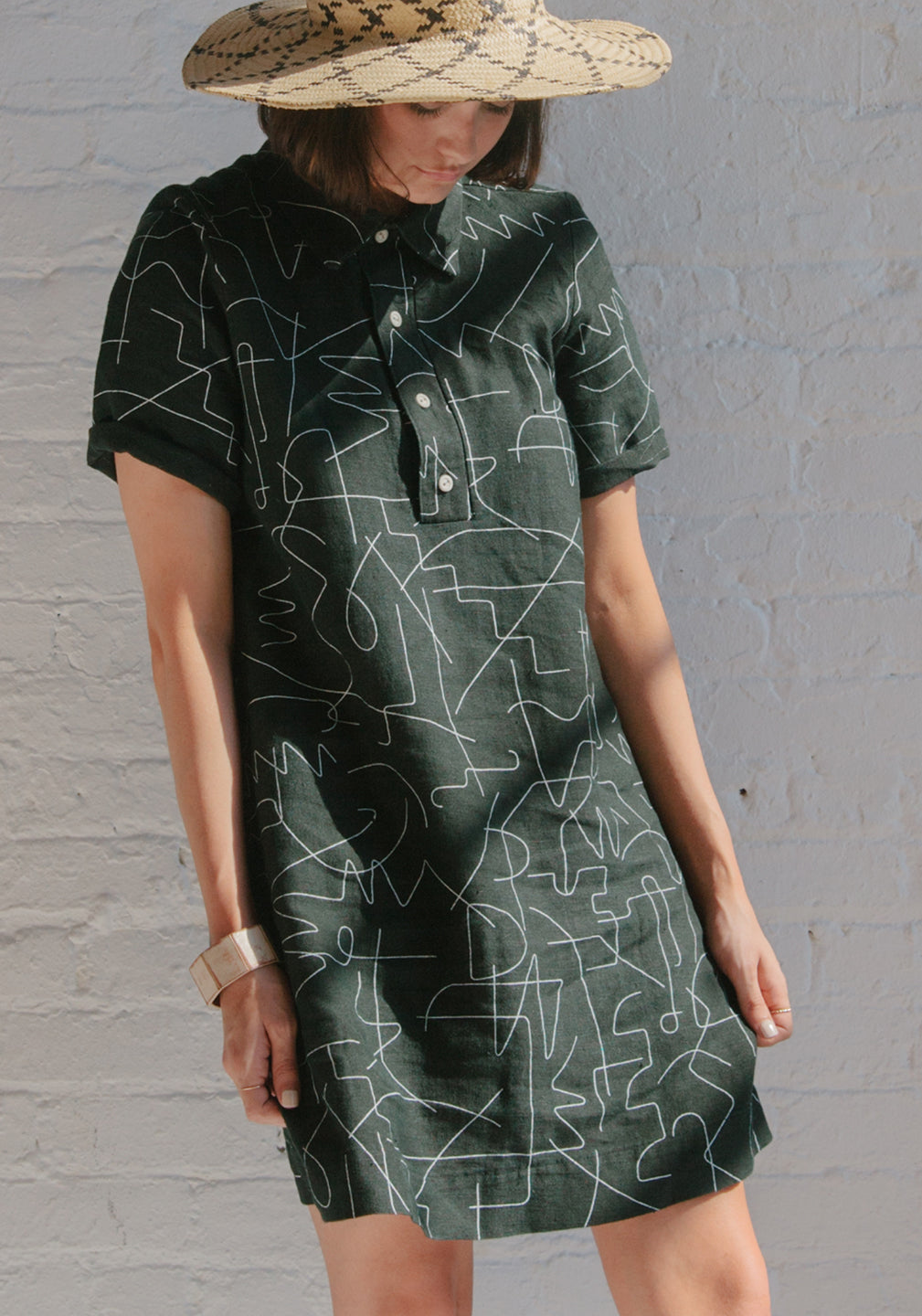 woman looking down in black short button up collared dress with white line pattern