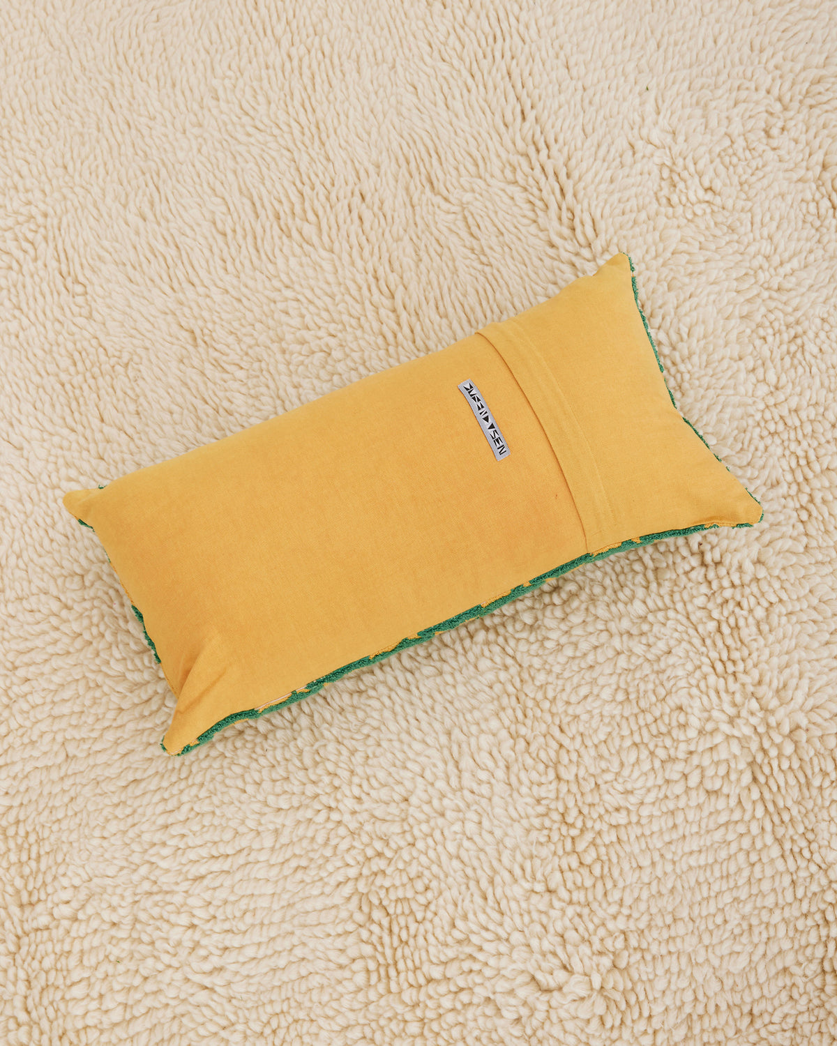100% cotton embroidery and tufting bolster pillow in green and mustard Sun pattern. Non-embroidered natural canvas back with a zipper opening. Available as 12" x 22". Spot clean only. Made in India.