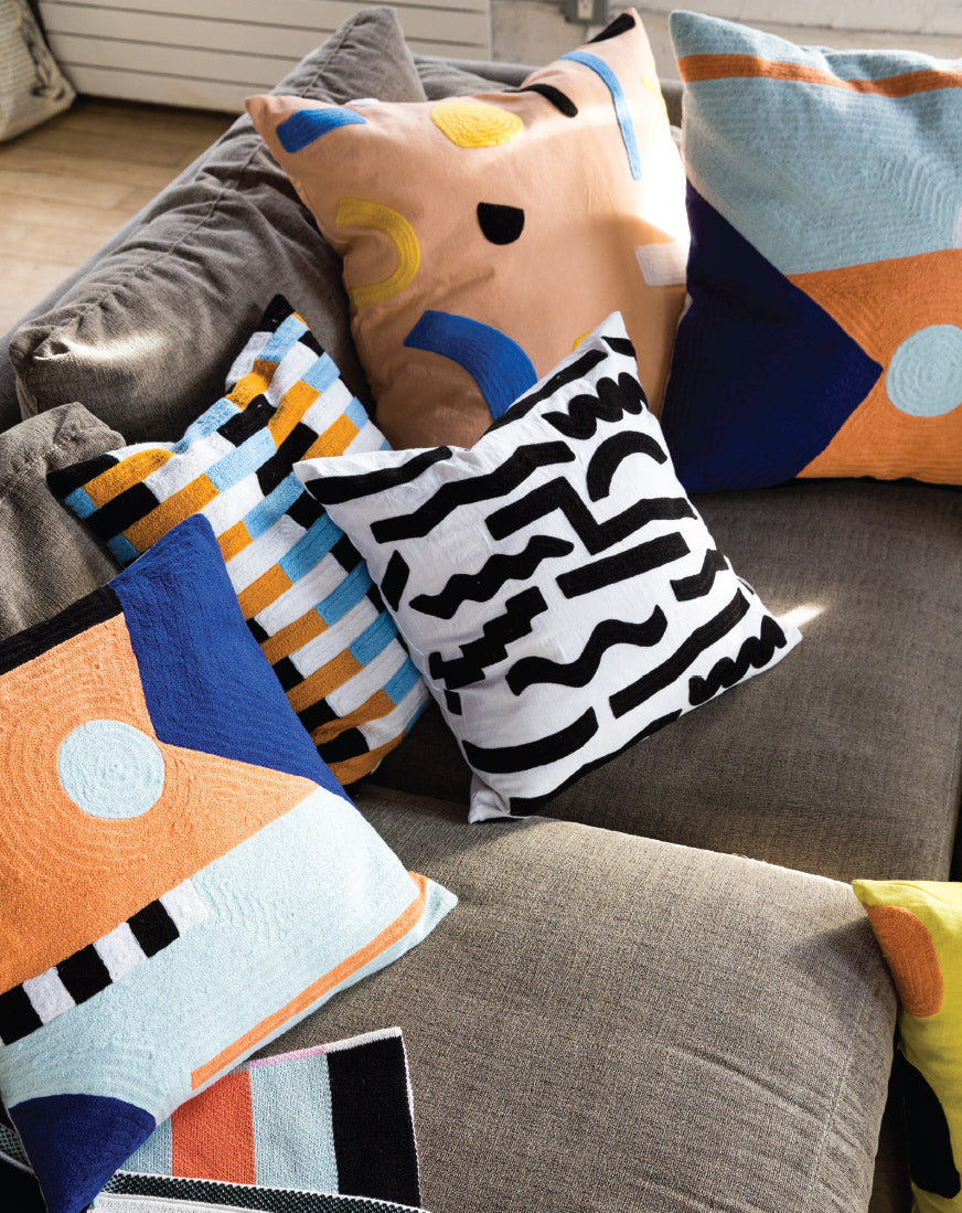 black and white pillow on couch surrounded by colorful pillows