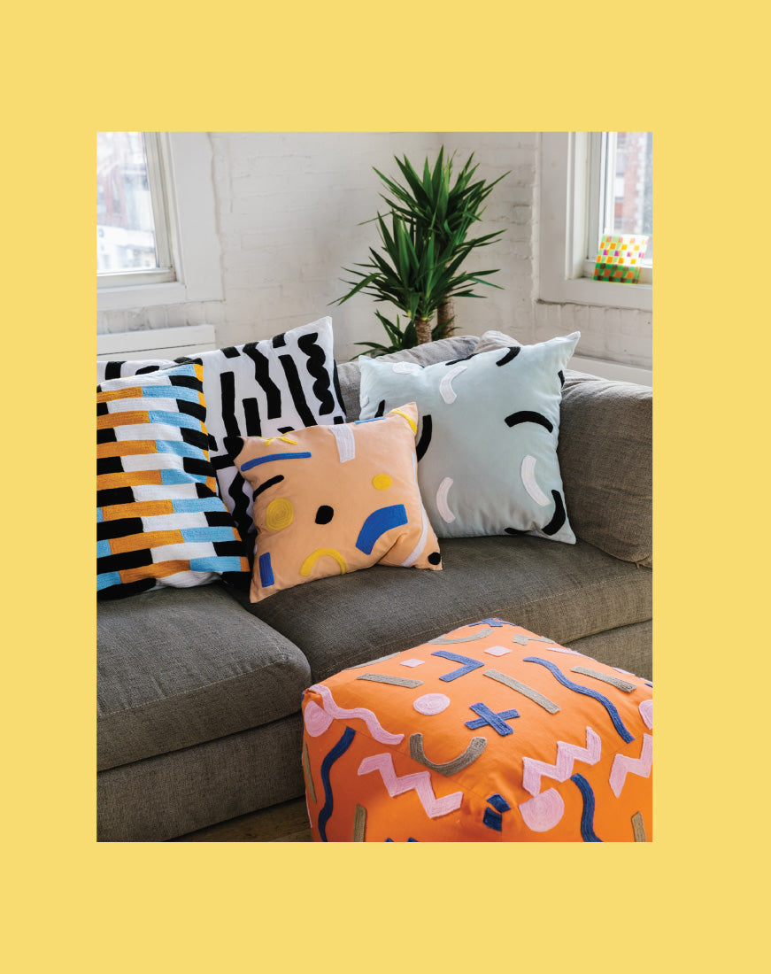 orange pouf with two pastel pillows on grey couch