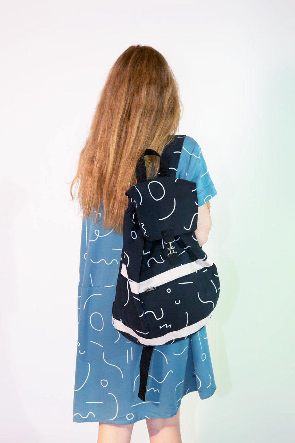 figure from behind with long hair and black satchel backack with white line pattern