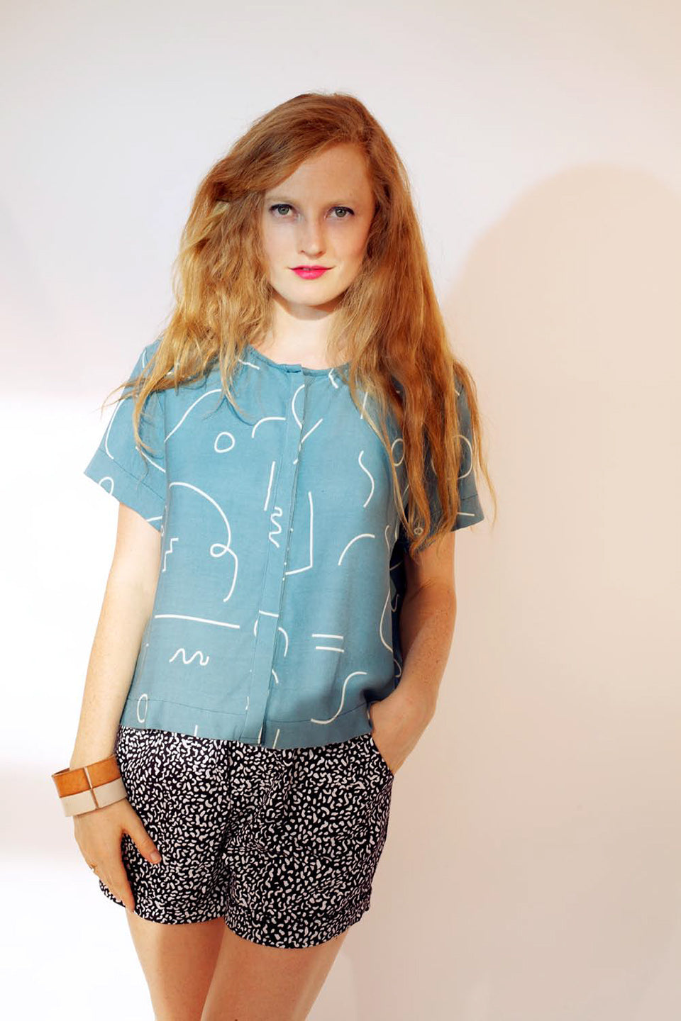 woman with black splatter pattern shirts with blue button up top and line patter in white hand in pocket