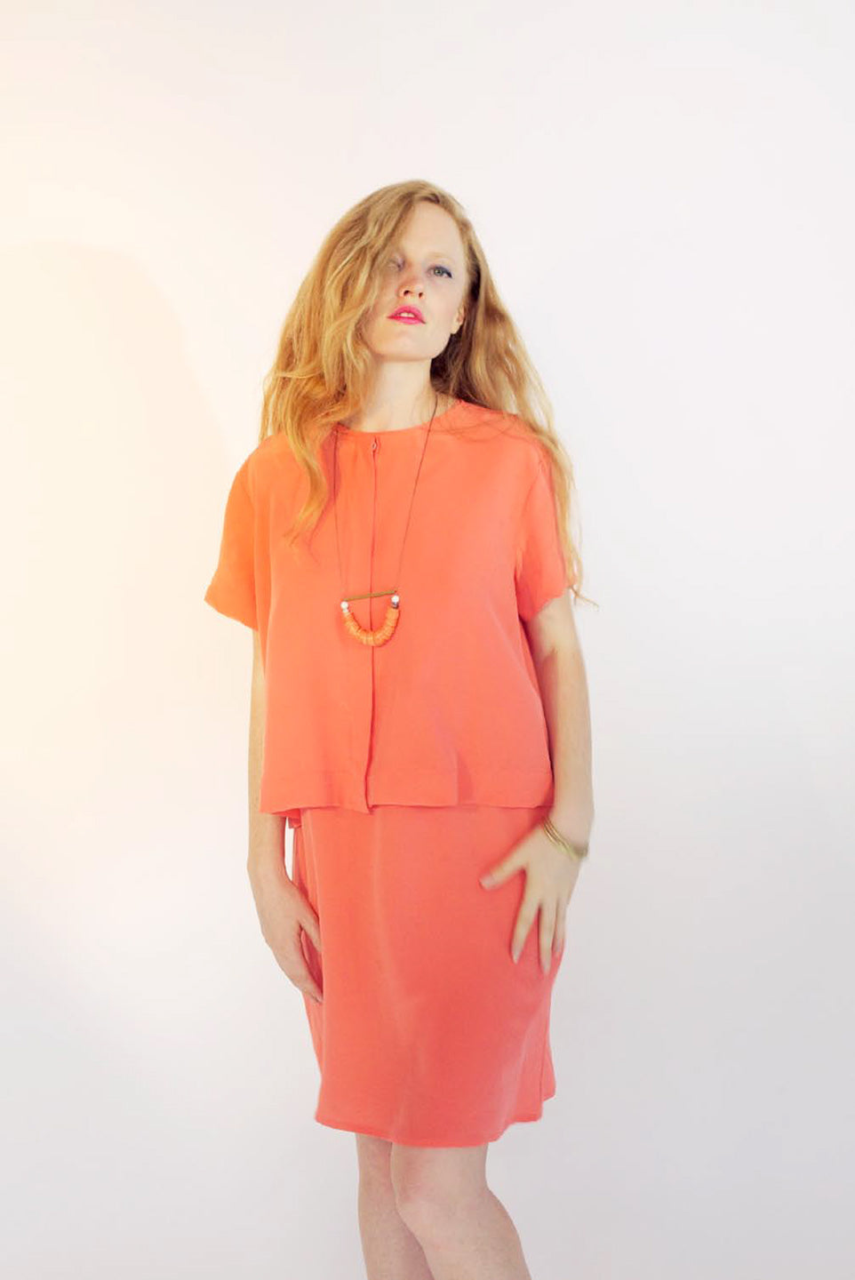 woman in orange shirt and skirt with pendant neckalce
