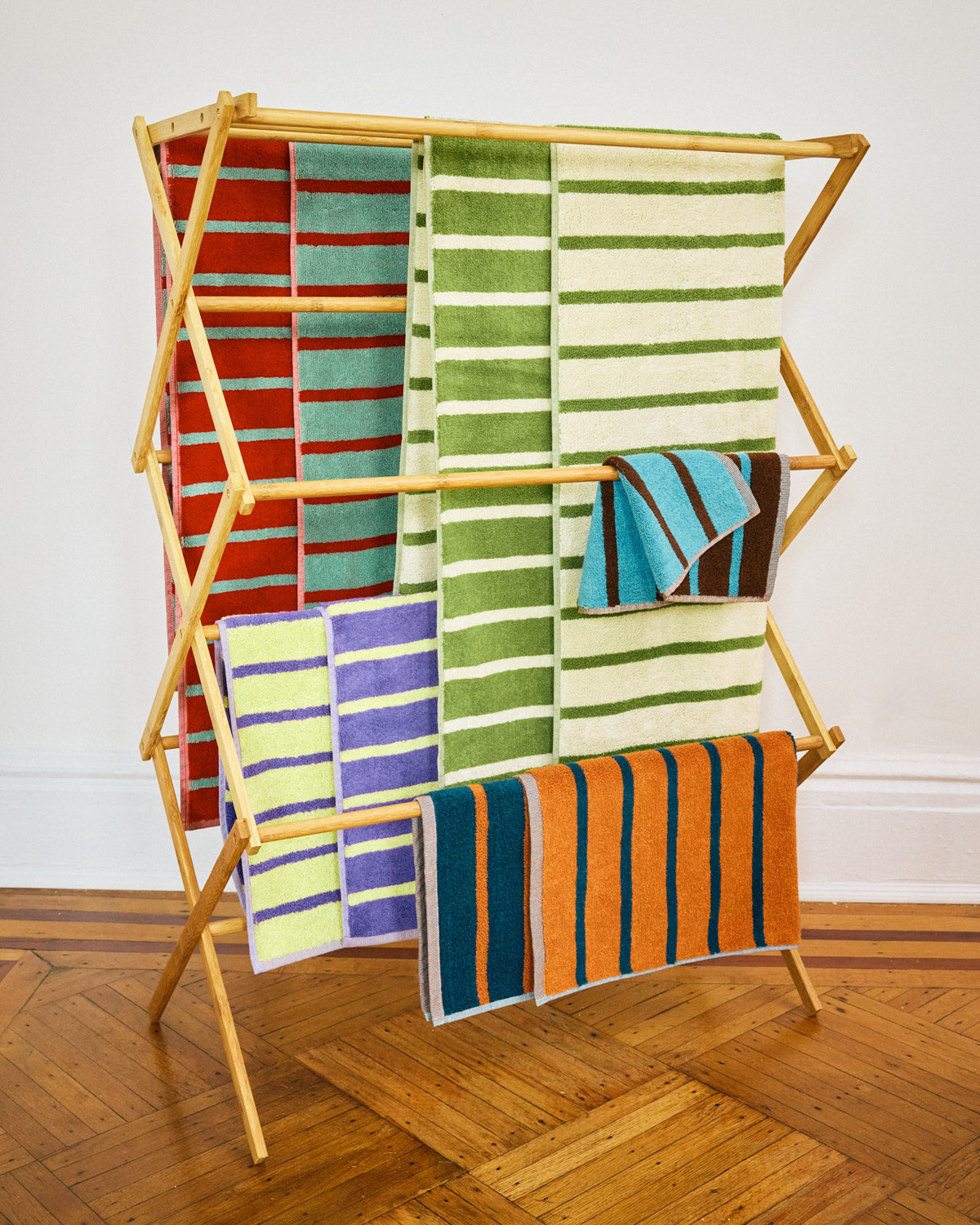 Five Dusen Dusen multiple stripe towels drape over drying rack on hardwood floor.