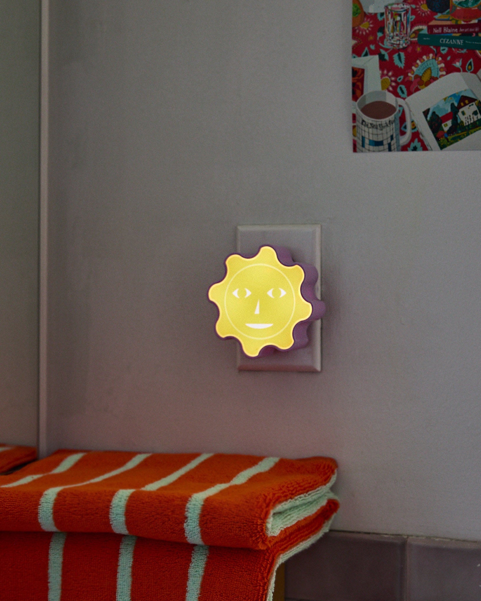 Dusen Dusen Yellow Sun nightlight glows in dark bathroom under stack of orange towels.