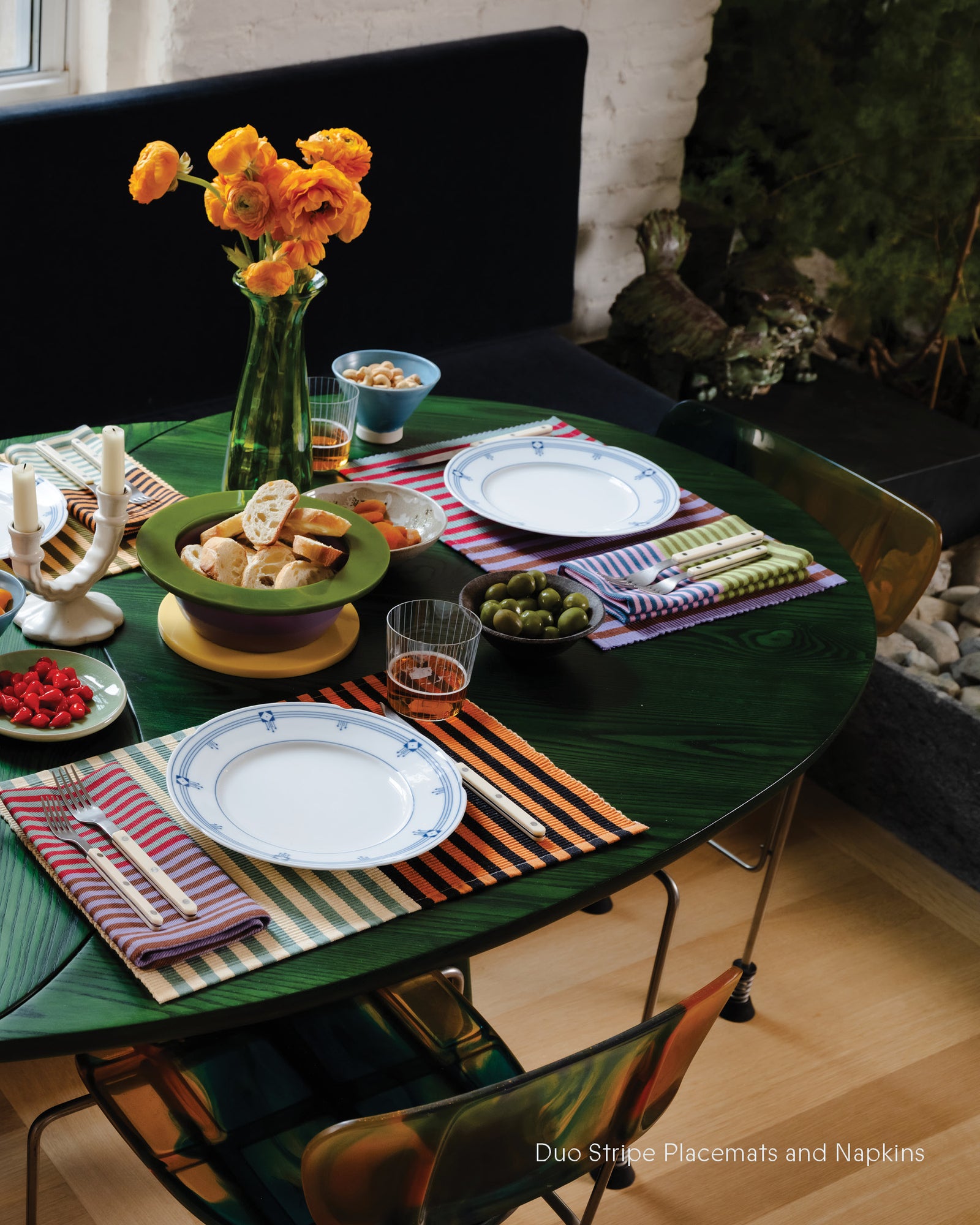 Dining table set with colorful placemats, plates, and a vase of flowers.