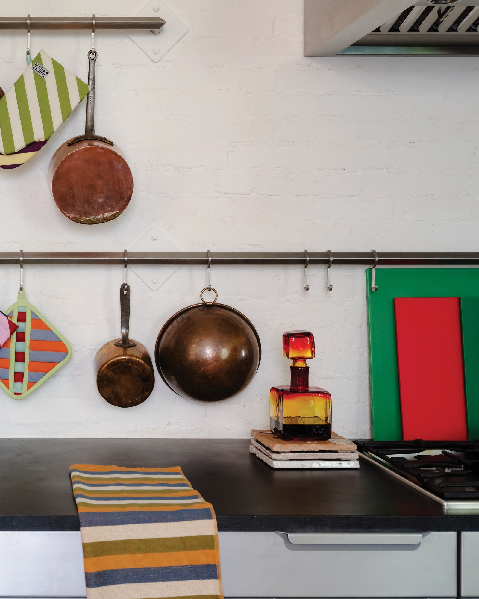 Kitchen counter with copper pots, colorful towels, and a bottle of whiskey.