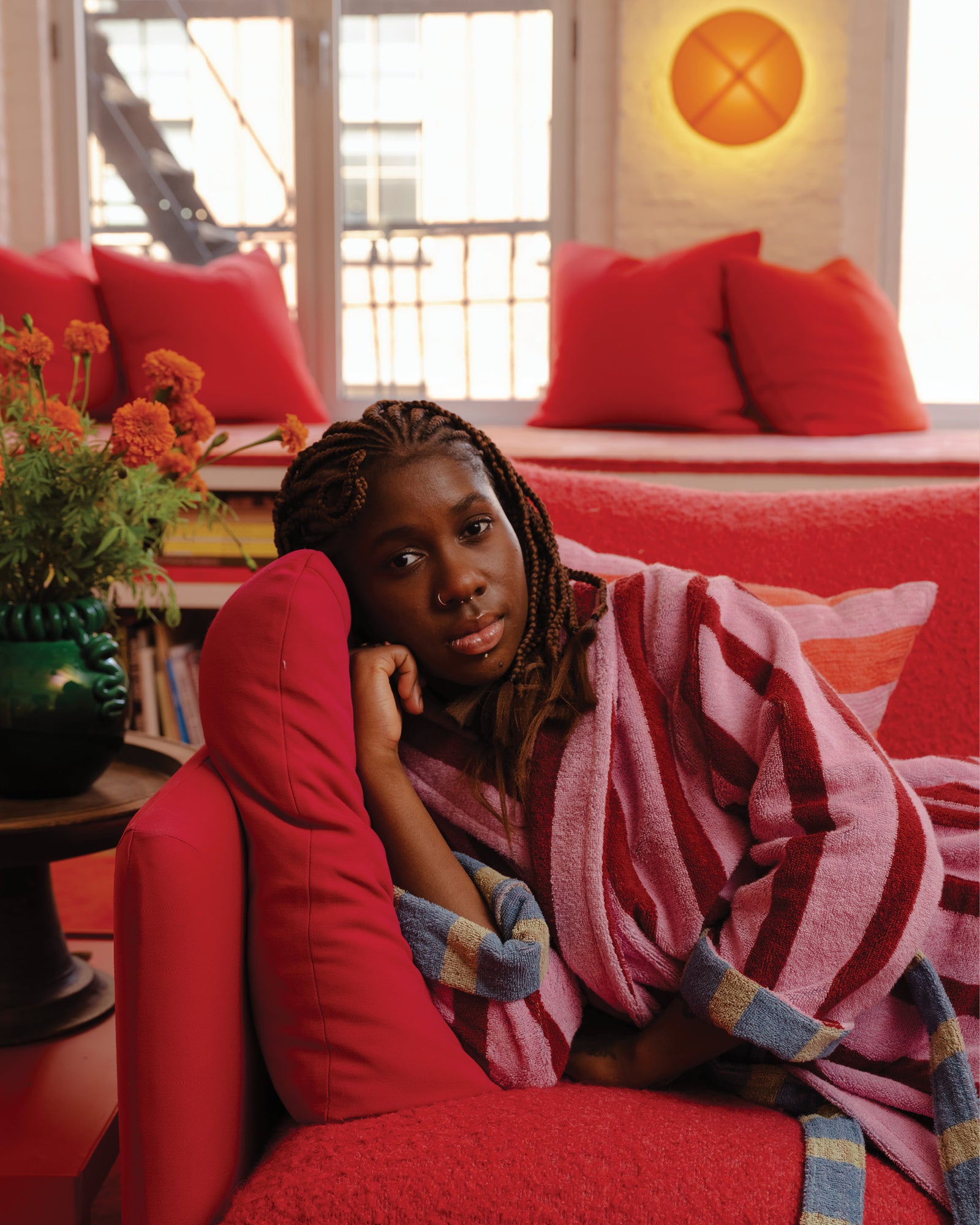 Person wrapped in a striped blanket sitting on a red chair in a room with red pillows and decor.