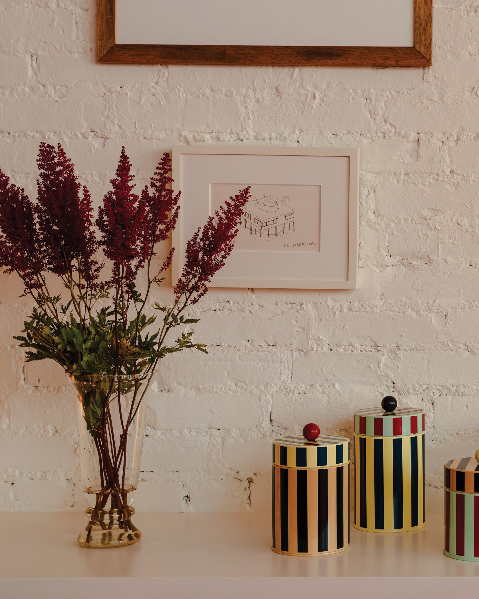Decorative canisters with striped patterns on a white surface against a white brick wall.