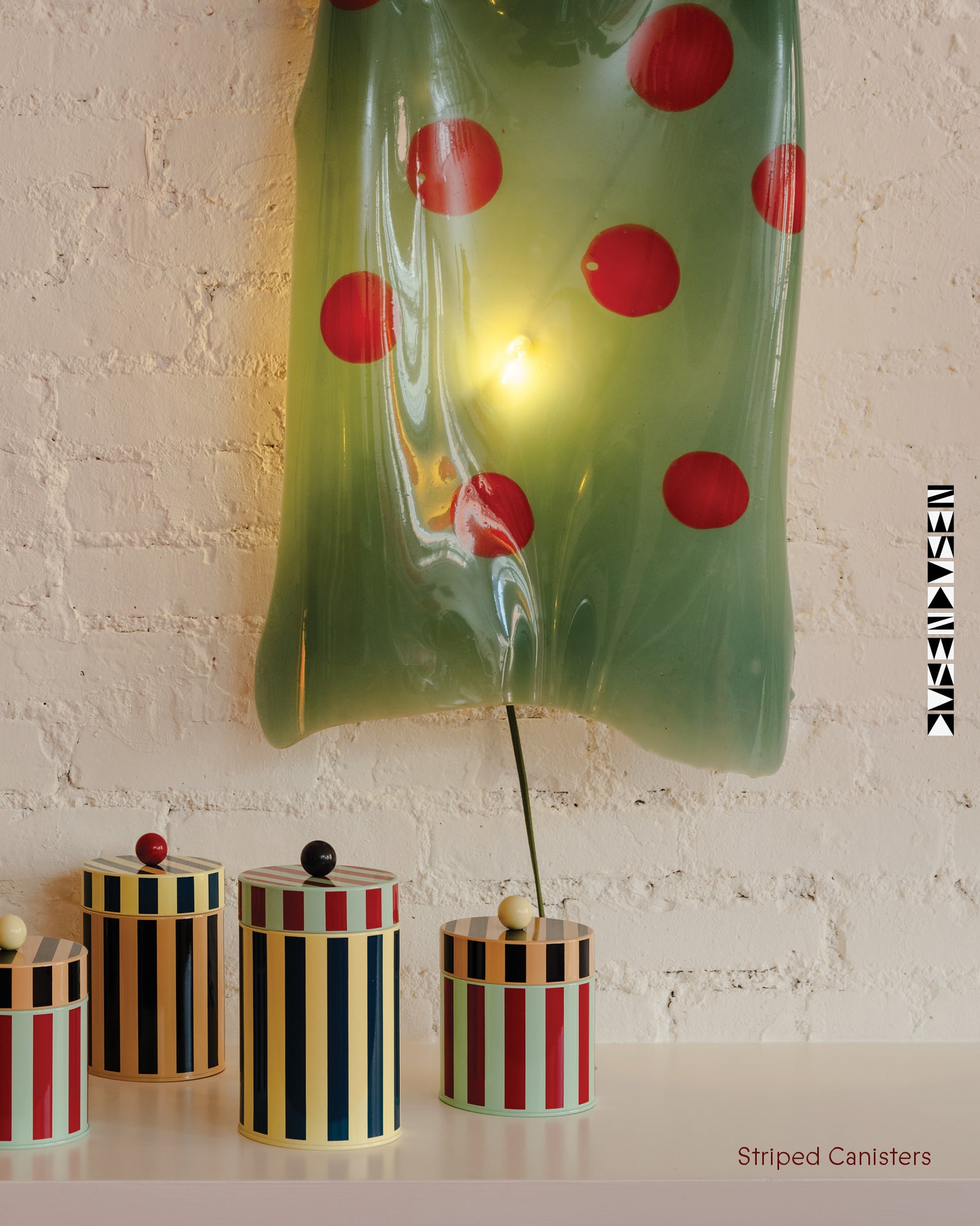 Decorative striped canisters with a green polka dot lamp against a light brick wall.