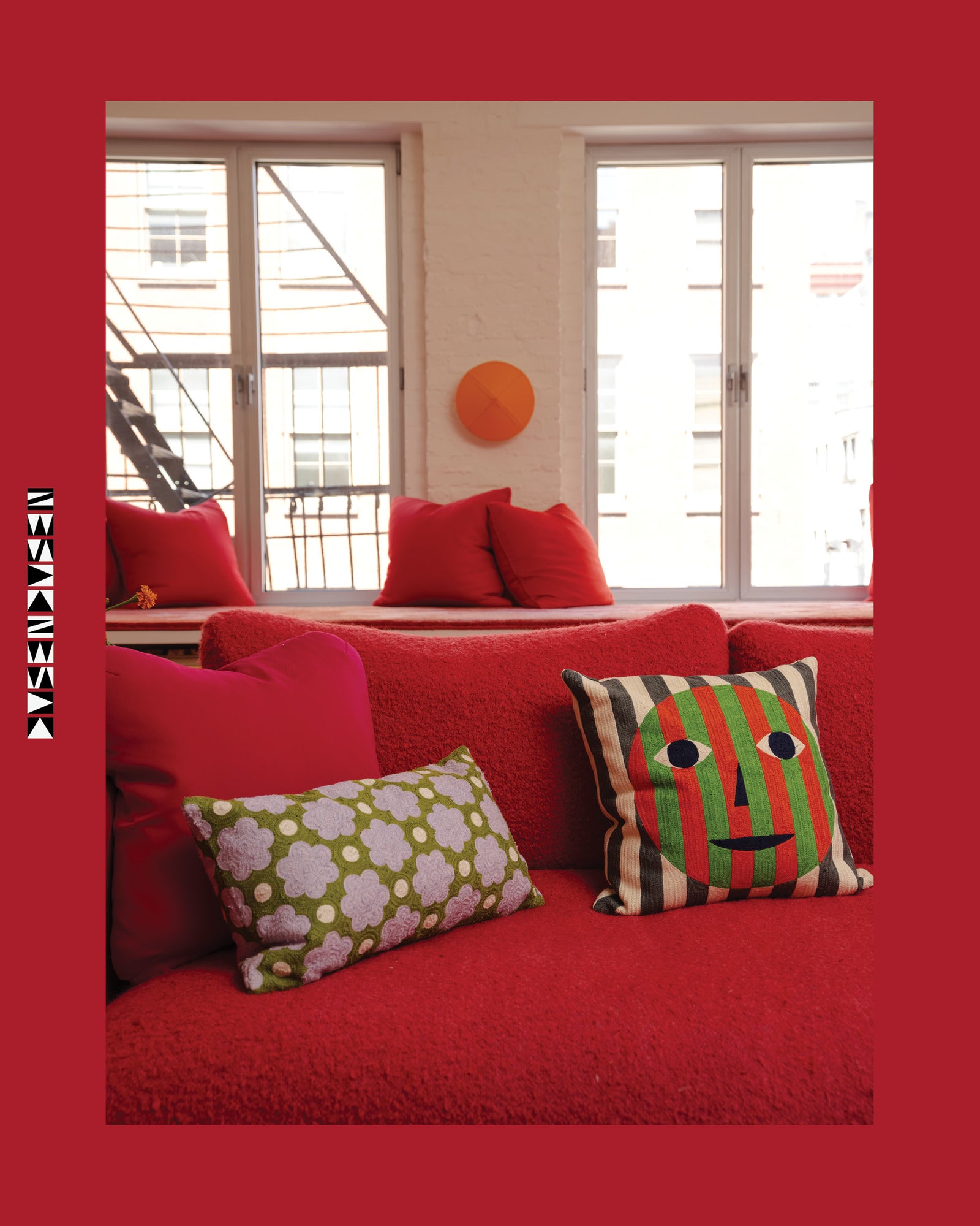 Red sofa with colorful cushions in a room with large windows.