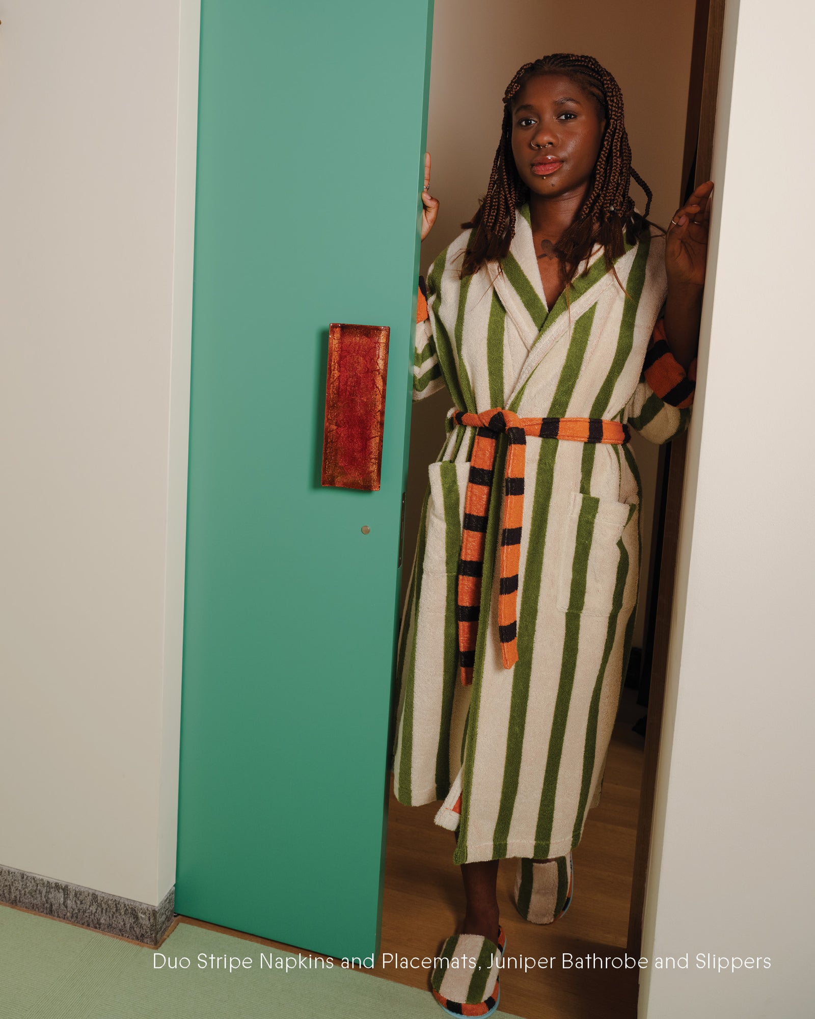 Woman wearing a striped robe standing in a doorway with a green wall.