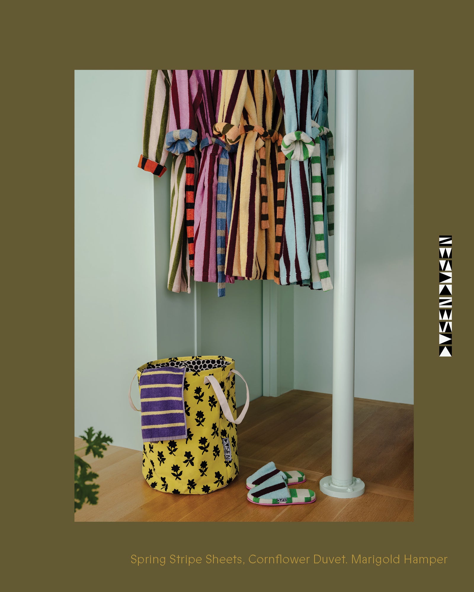 Colorful striped sheets, cornflower duvet, and marigold hamper on a rack against a white wall.