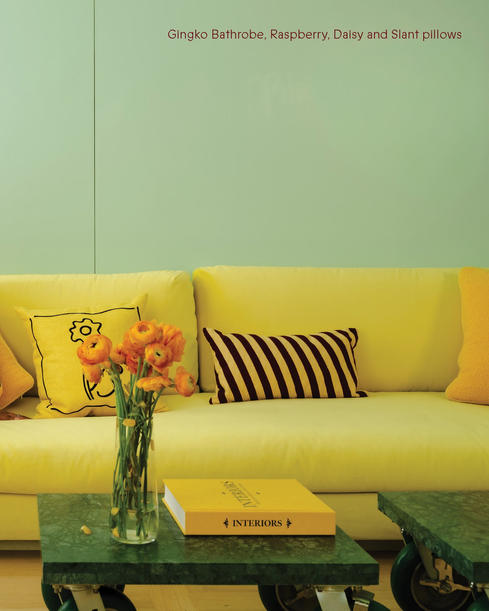 Yellow sofa with decorative pillows and a vase of flowers on a green table.