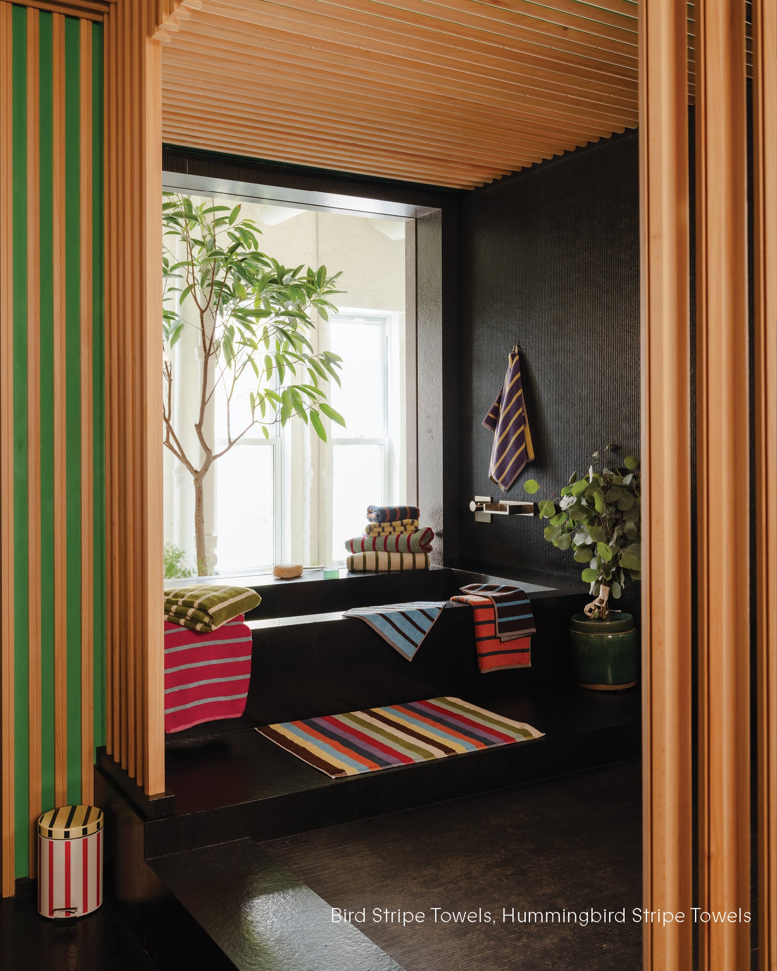 Bathroom interior with striped towels and plants, featuring a window and wooden ceiling.