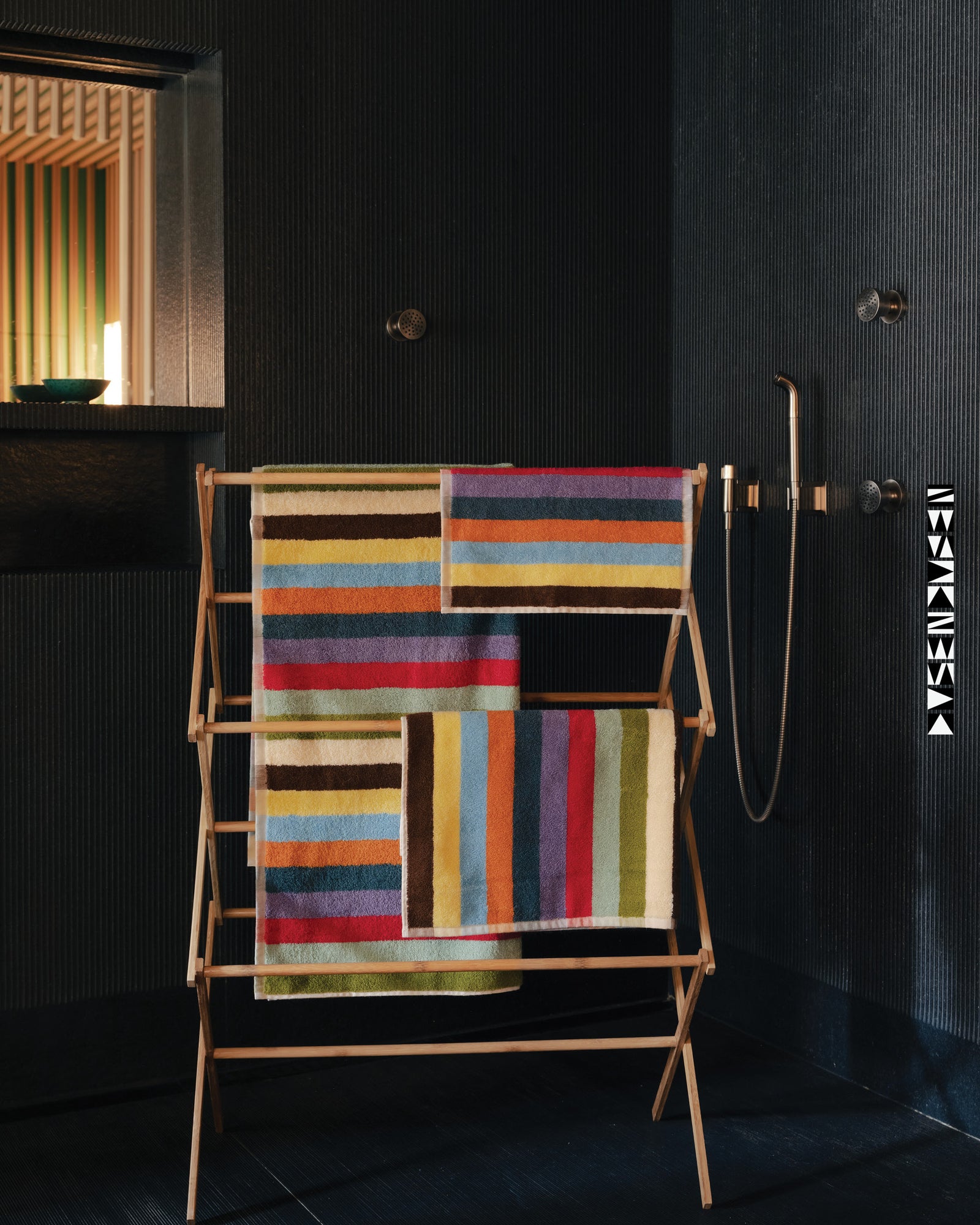 Colorful striped towel on a wooden rack against a dark wall.