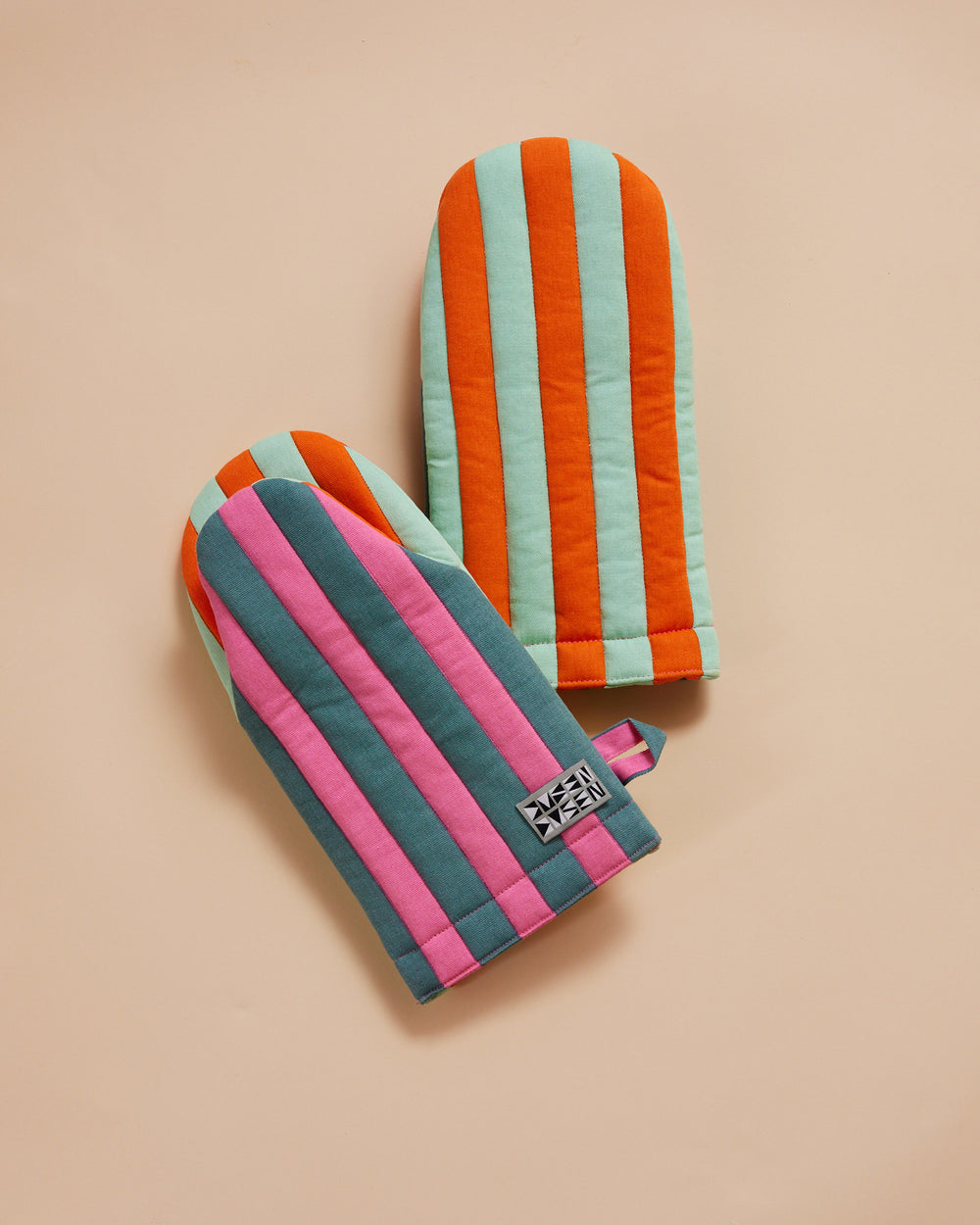 Dusen Dusen Ginger Oven Mitt in Pink, Blue Grey, Orange and Teal. Padded oven mitt in varying stripe weights and contrasting stripe colorways. Features a "frog-style" mitt shape, top stitched brand label, and a side loop. 100% cotton quilted canvas base, with polyester fill.