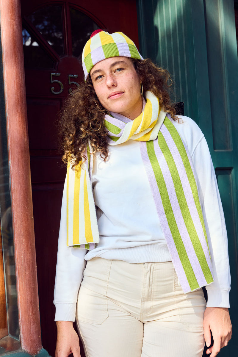 Squash Stripe Hat. Ribbed-knit pom beanie with contrasting yellow, white, lilac, and green stripes. 100% Cotton. Made in China.