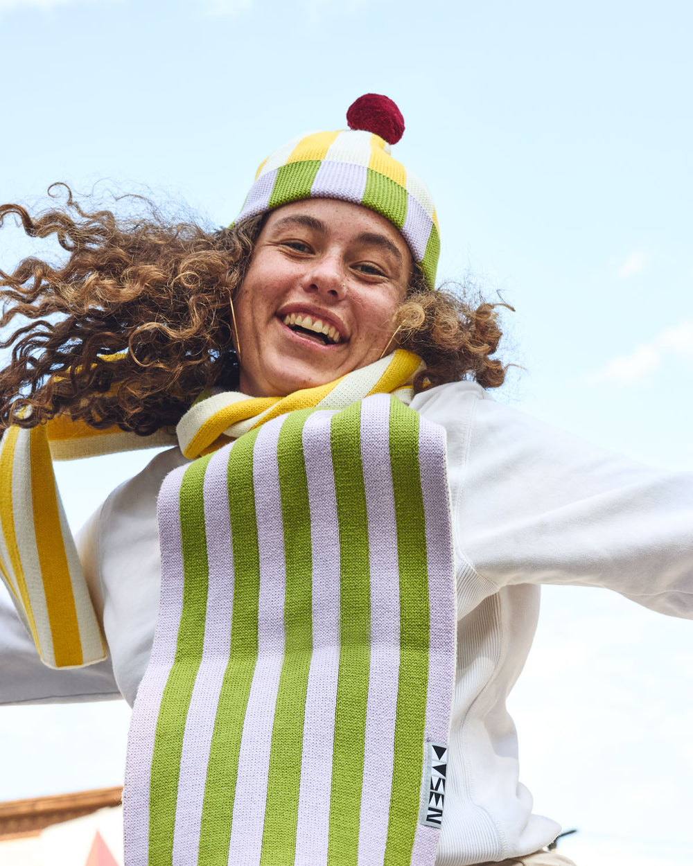 Squash Stripe Hat. Ribbed-knit pom beanie with contrasting yellow, white, lilac, and green stripes. 100% Cotton. Made in China.