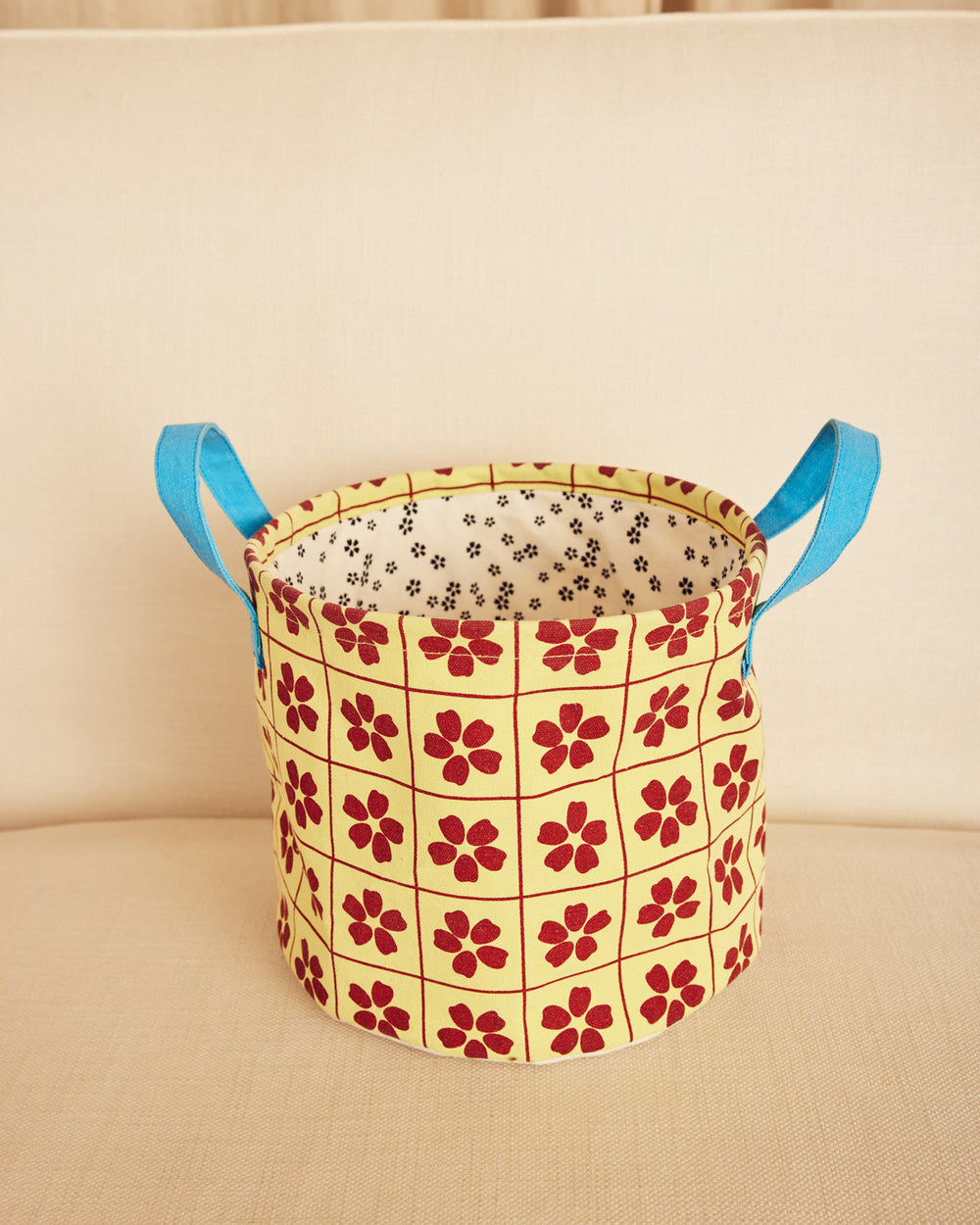 Floral-patterned storage basket with blue handles on a beige background