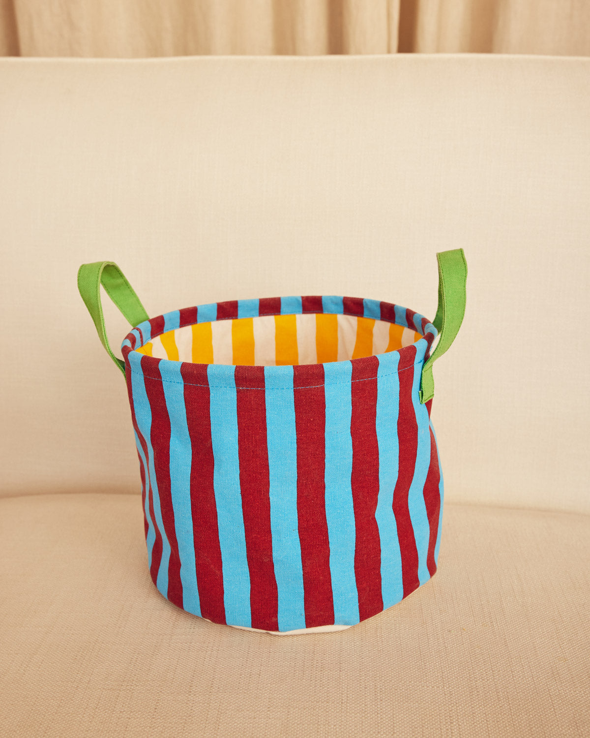 Colorful striped storage basket with green handles on a beige surface