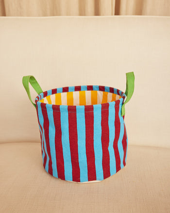 Colorful striped storage basket with green handles on a beige surface