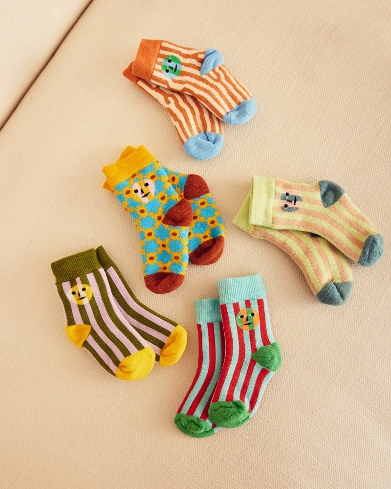 ["Set of 5 socks with 3 stripes and two patterns on a beige couch"]