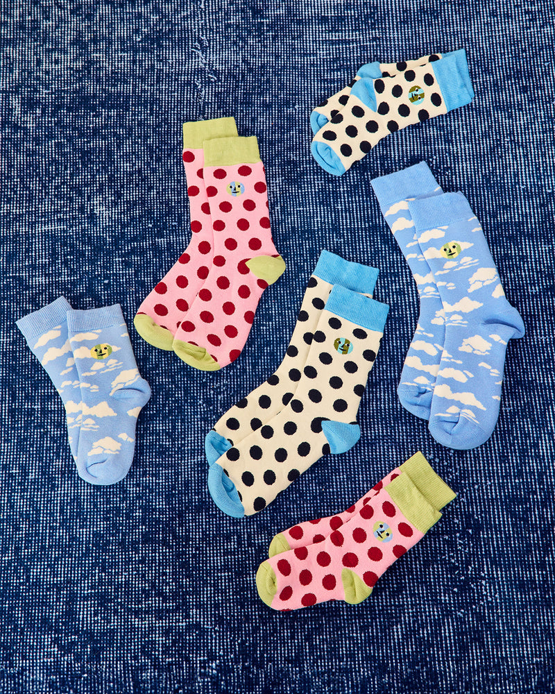 Six pairs of children's socks in various colorful patterns (polka dots, clouds, and black spots on cream) are arranged on a textured blue background.