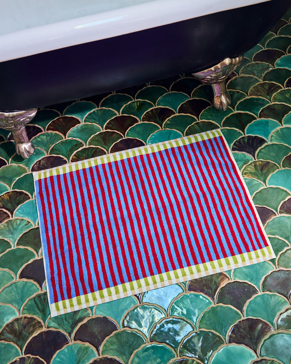 Red and blue striped towel on a green tiled bathroom floor